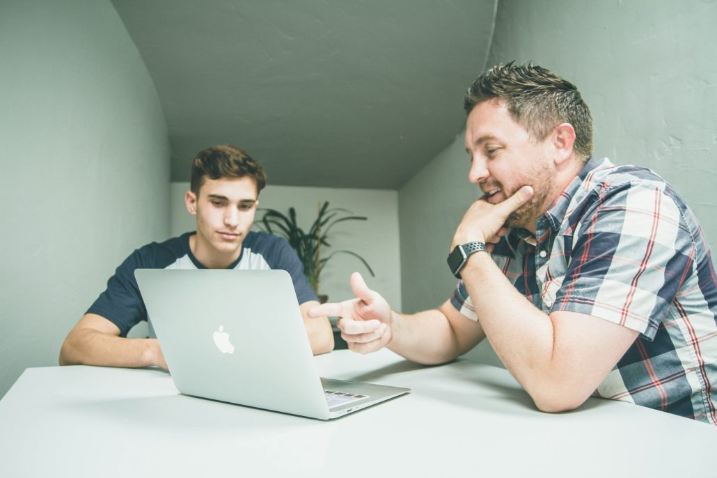 Two men are looking at a laptop and talking.