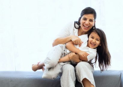 A mom with dark hair is holding her daughter on her lap, they are both smiling