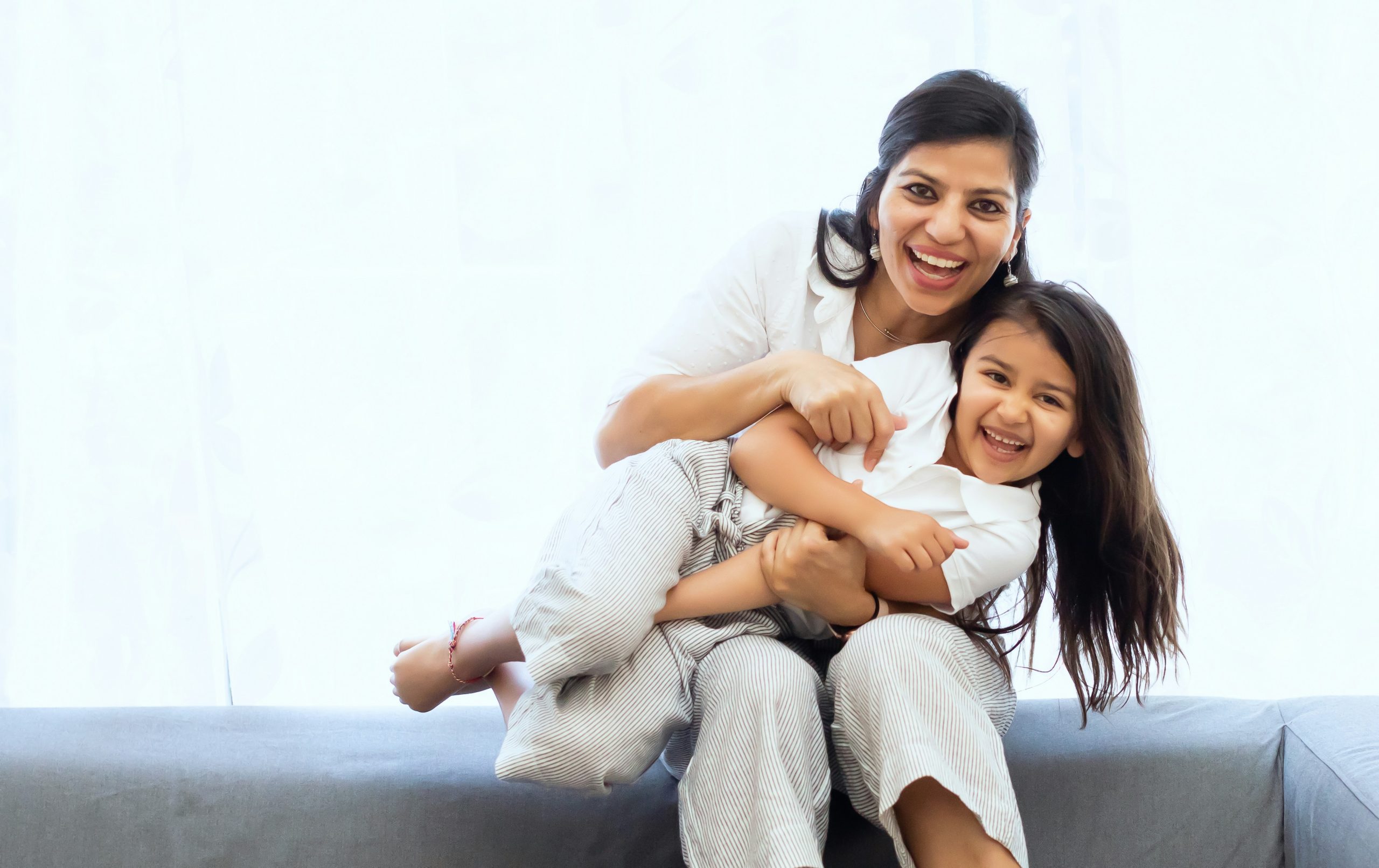 A mom with dark hair is holding her daughter on her lap, they are both smiling