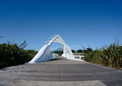 White sculptural bridge in the middle of a bath with flax on the left and right.