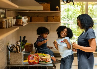 Two young children are smiling and playing in the kitchen with their mom
