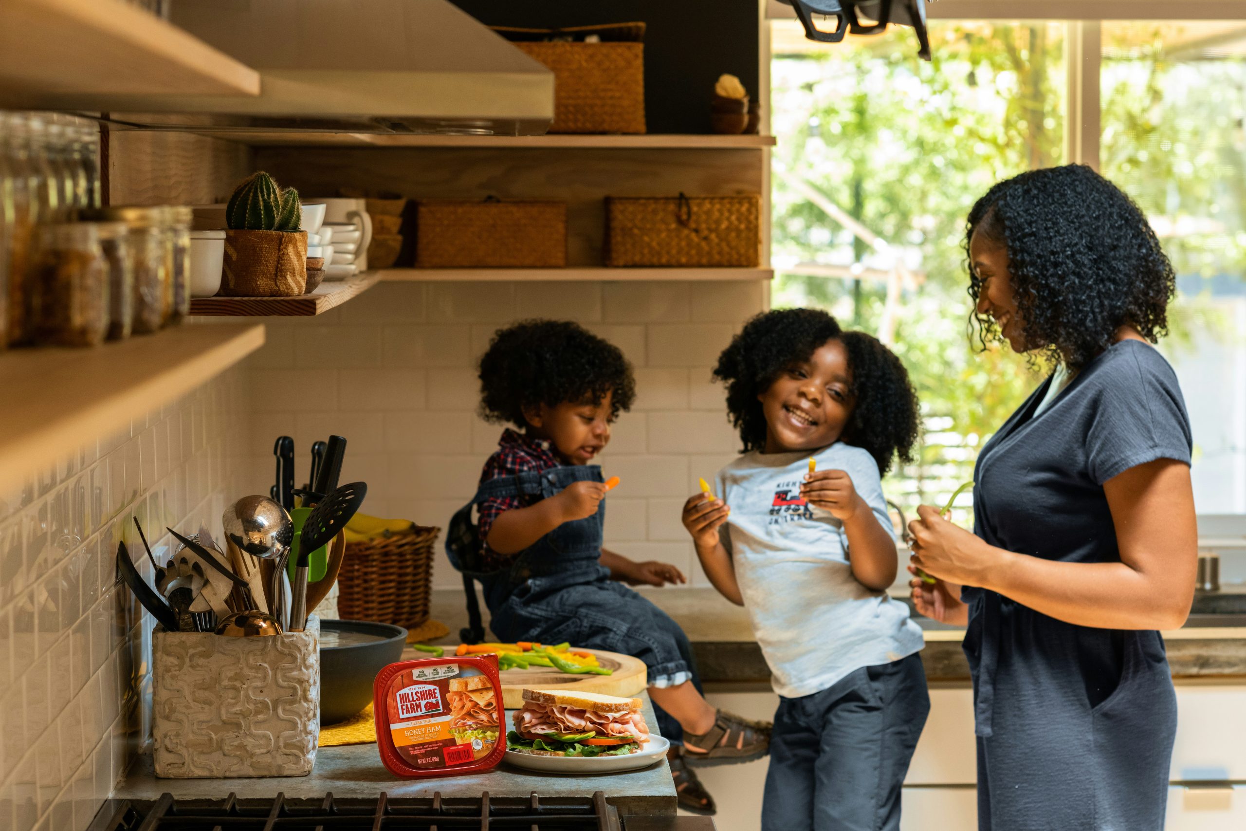 Two young children are smiling and playing in the kitchen with their mom