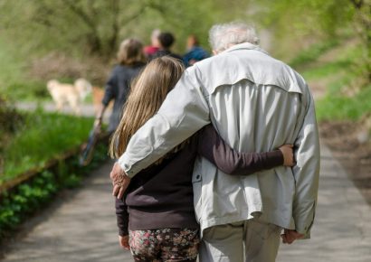 The backs of a young girl and older man walking with their arms around each other.