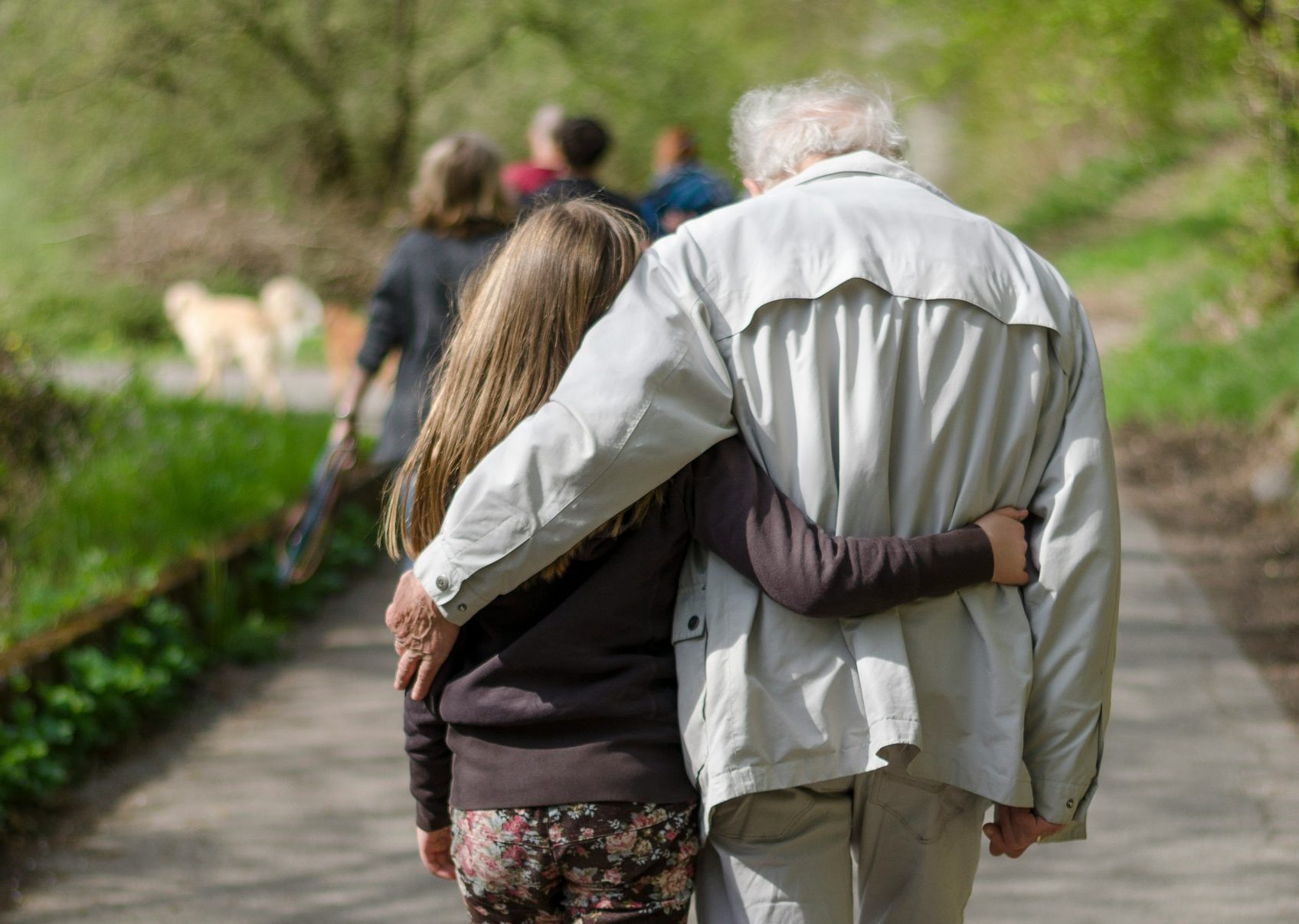 The backs of a young girl and older man walking with their arms around each other.