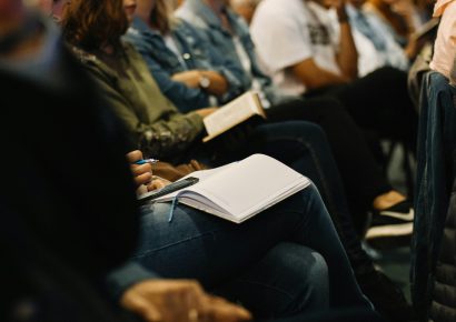 A row of people sitting, some have notebooks on their lap