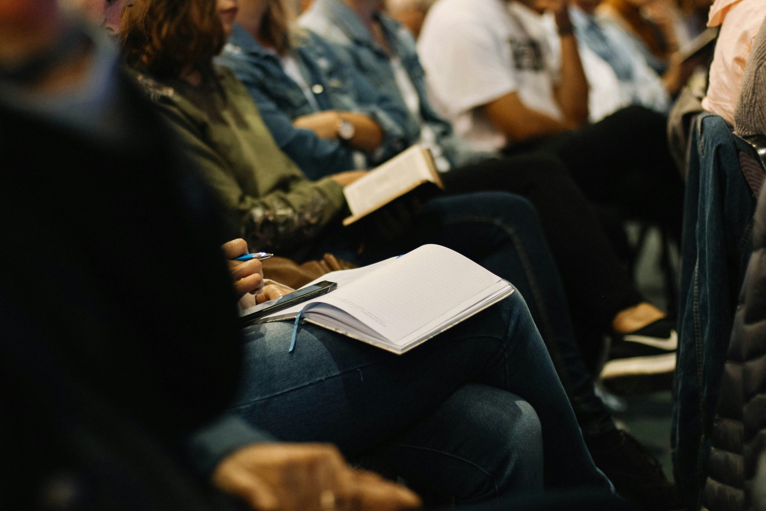 A row of people sitting, some have notebooks on their lap