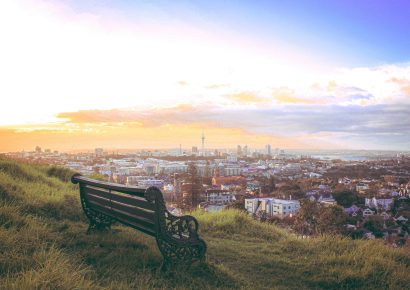 View of the Auckland cityscape with a bench on a grassy hill at the front