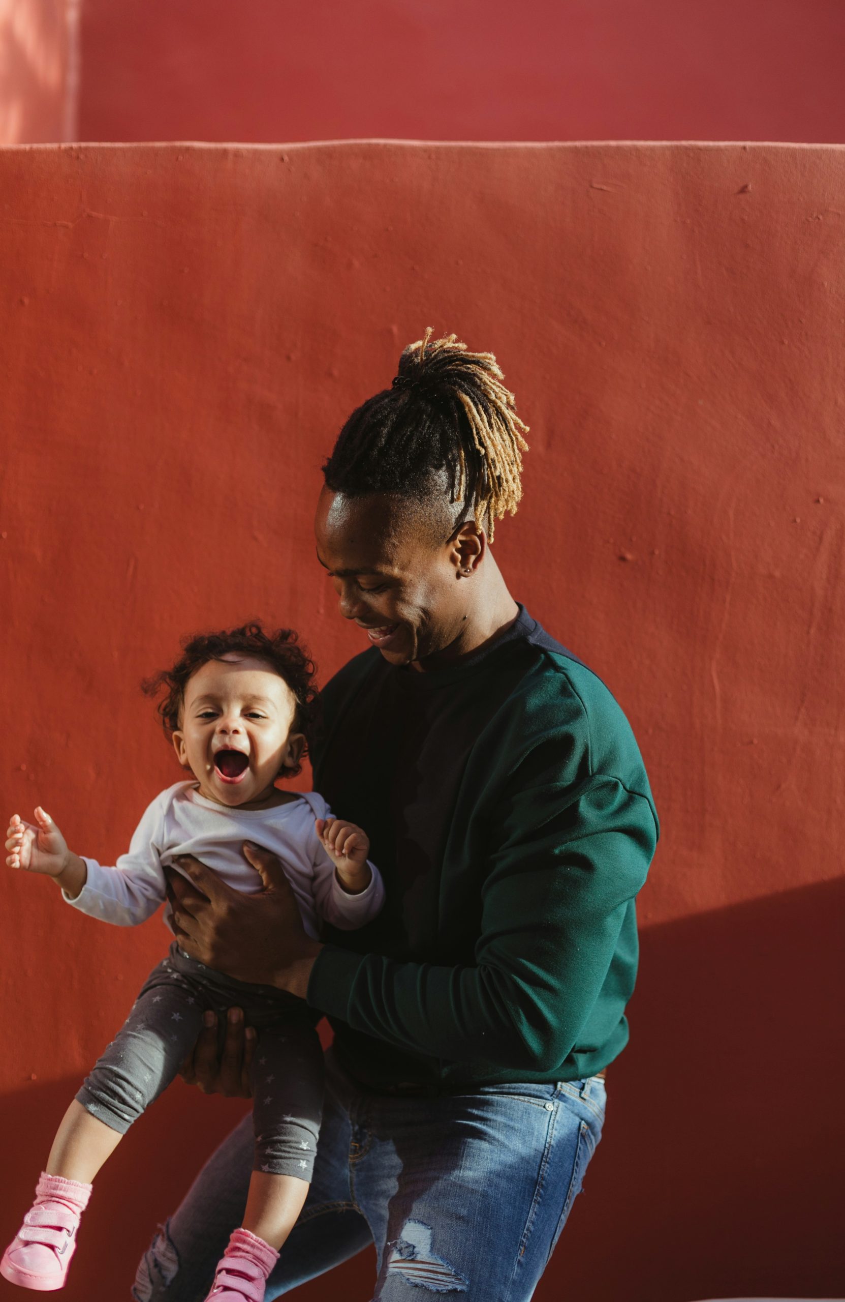 A dad is holding and playing with their baby. They are both smiling